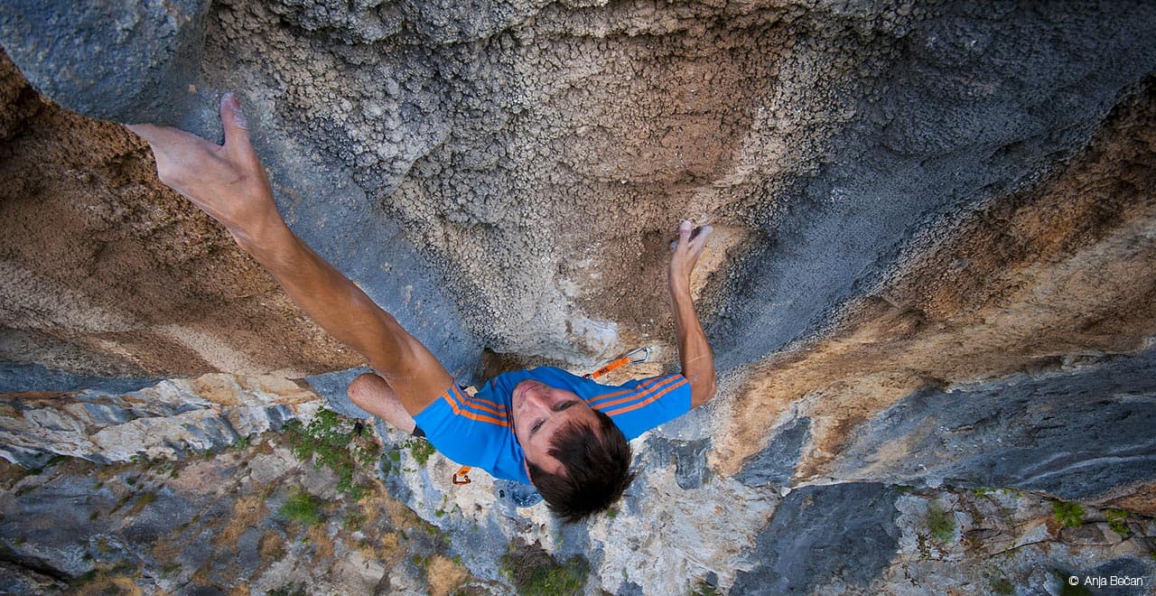 Klemen Bečan climbing a steep orange limestone roof – Rockbusters coach interview