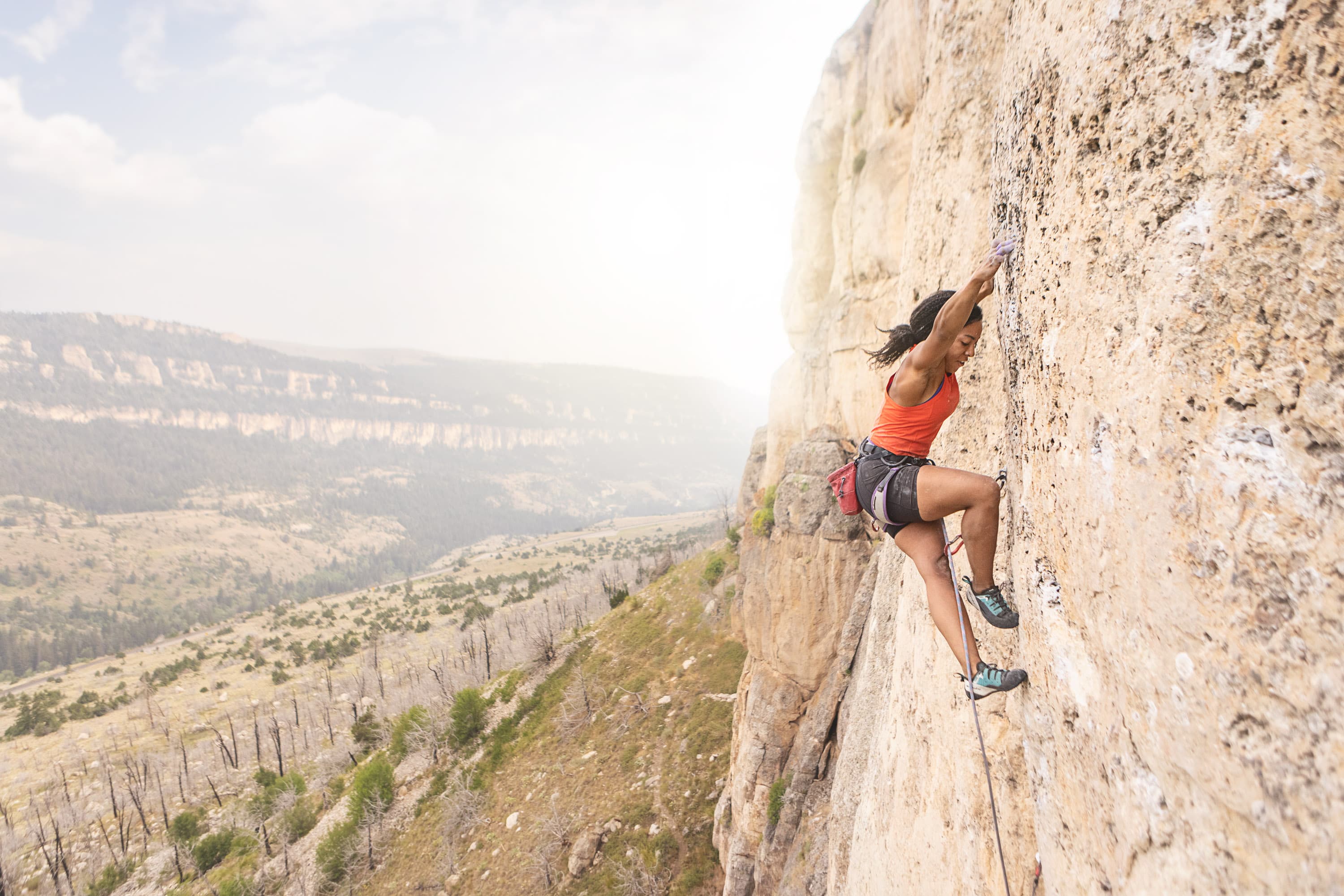 Woman climbing a sunny limestone wall above a wide valley – Rockbusters climbing shoe guide