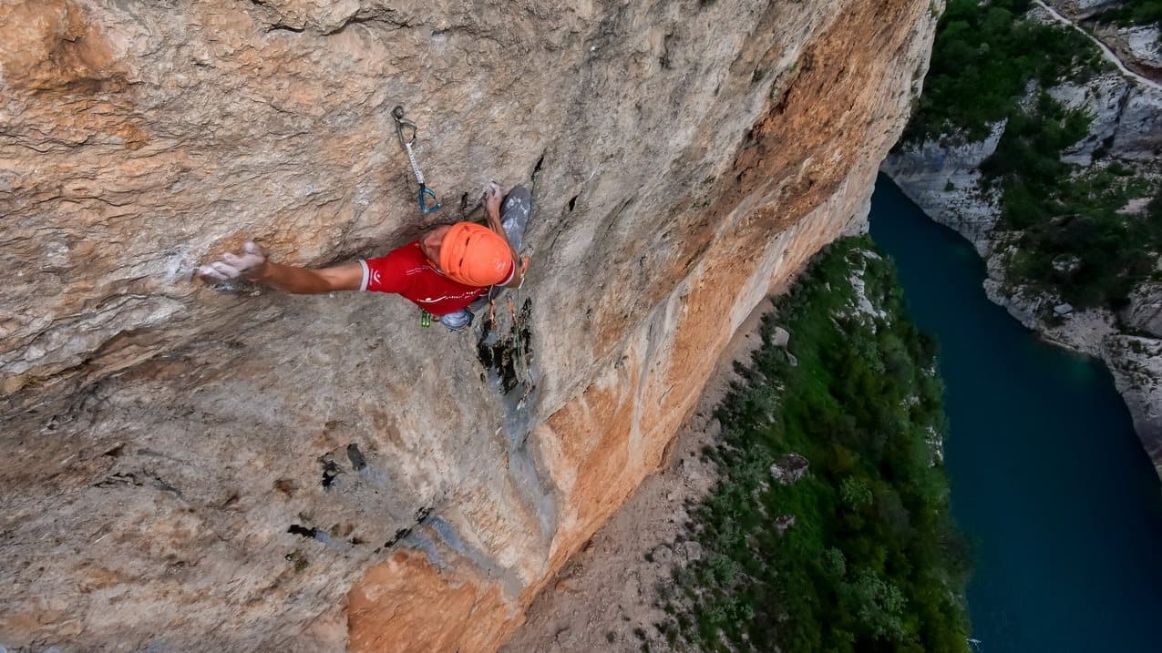 Klemen Bečan in a red helmet on orange limestone above a river – Rockbusters coaching