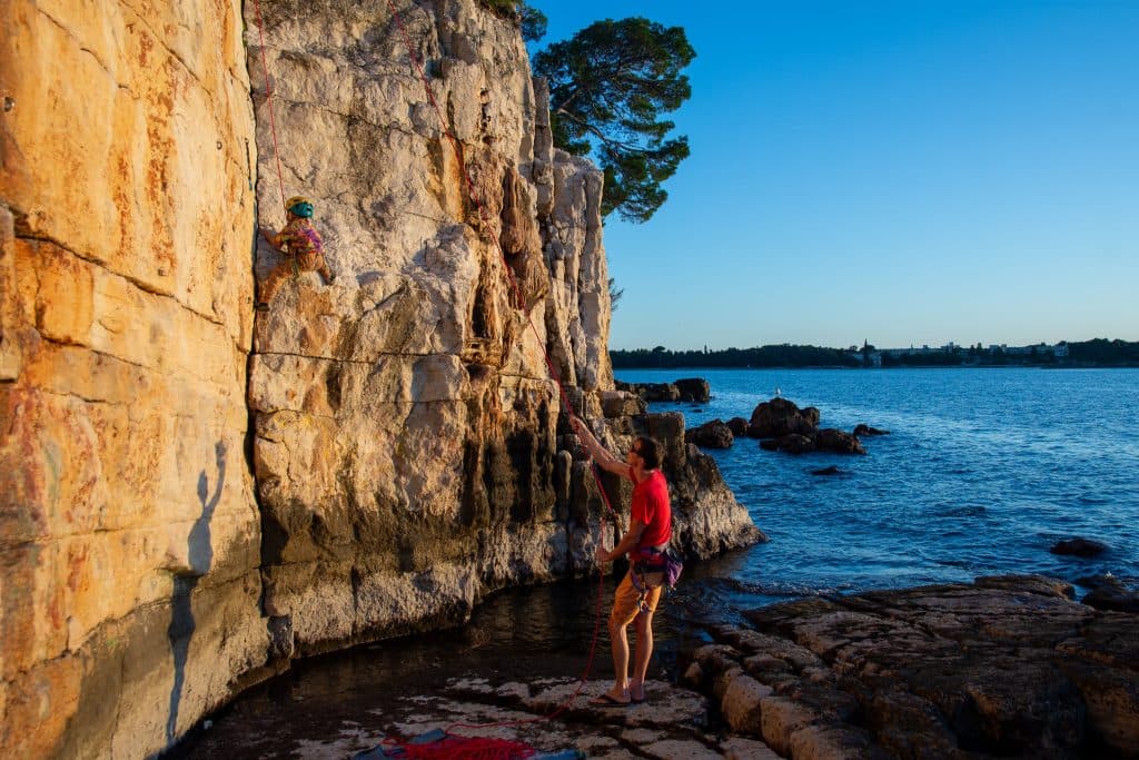 Climbers on sunlit sea cliffs by clear water near Rovinj, Istria, Croatia – Rockbusters climbing camp